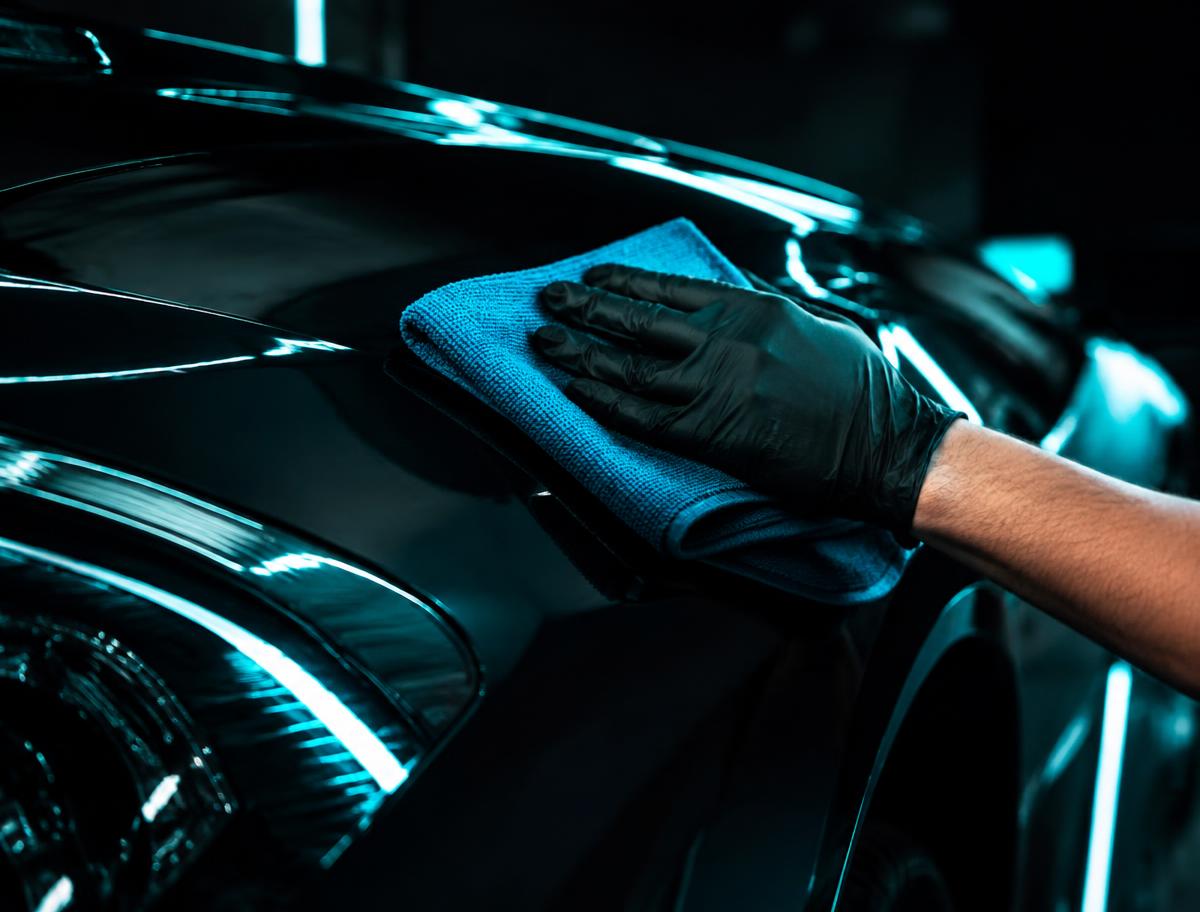 Detailer polishing a dark car panel with a microfiber cloth